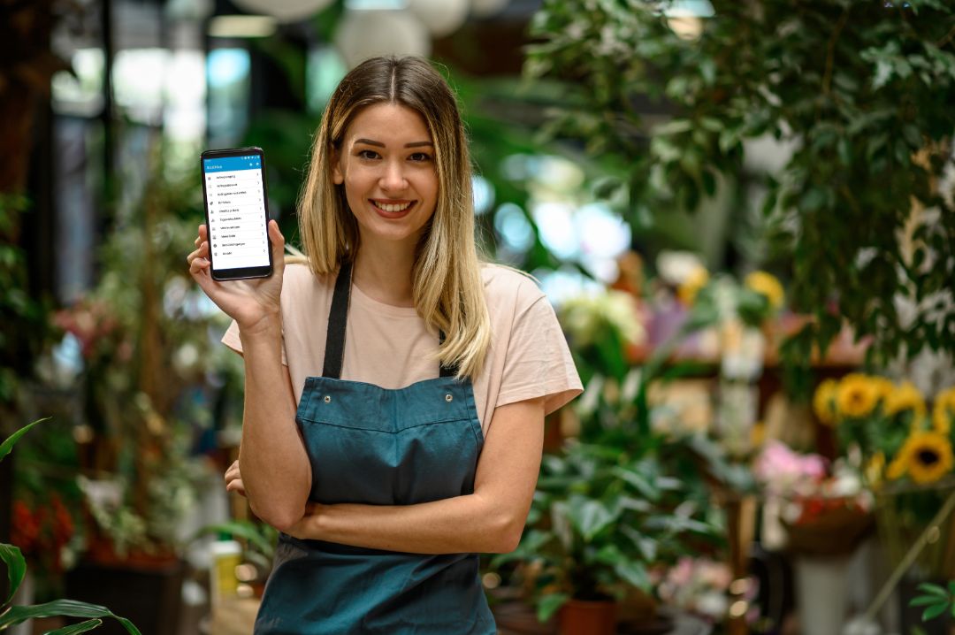 Florist showing a smartphone while surrounded with flowers and plants in a flower shop