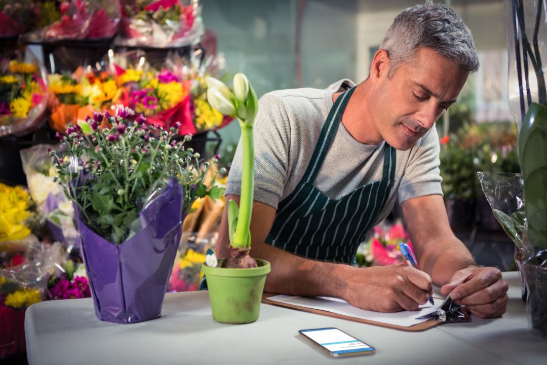 Male florist writing on clipboard at his flower shop