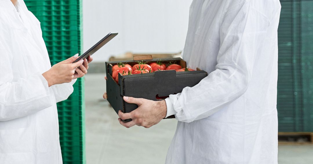 Side view of a smiling woman with a tablet computer standing next to a warehouse worker