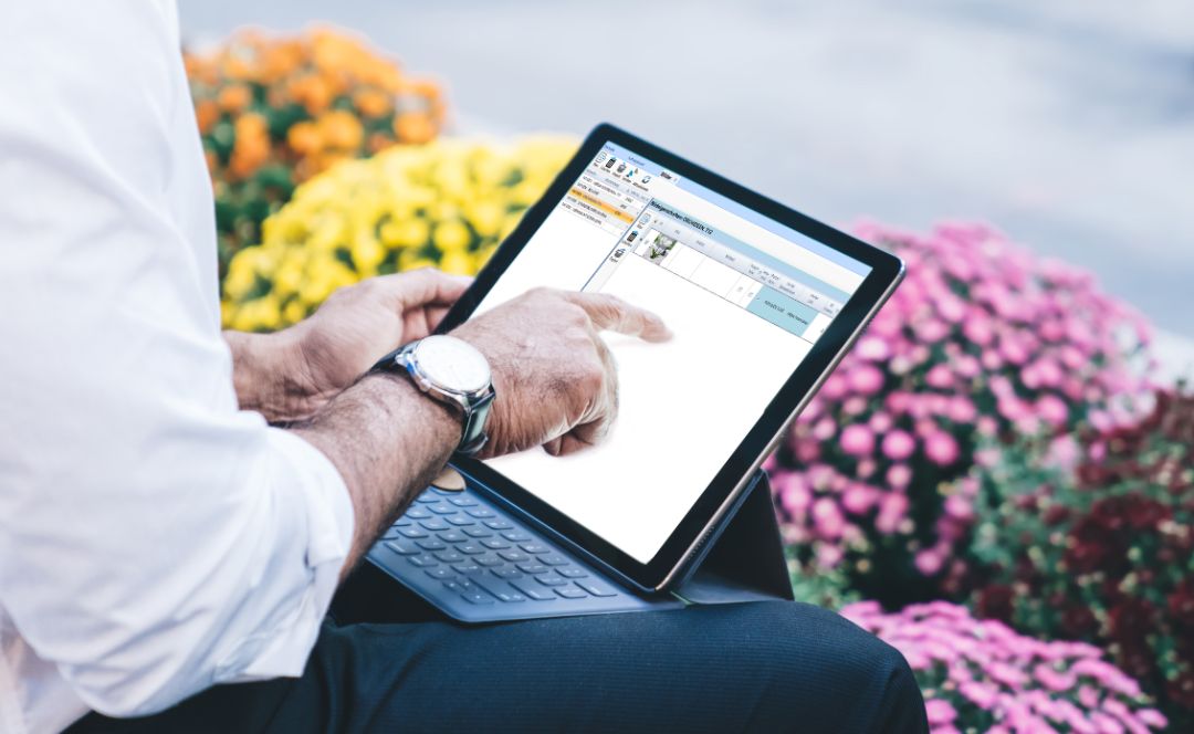 Side view of unrecognizable African American male office worker in white shirt working on tablet with keyboard on street near flowerbed