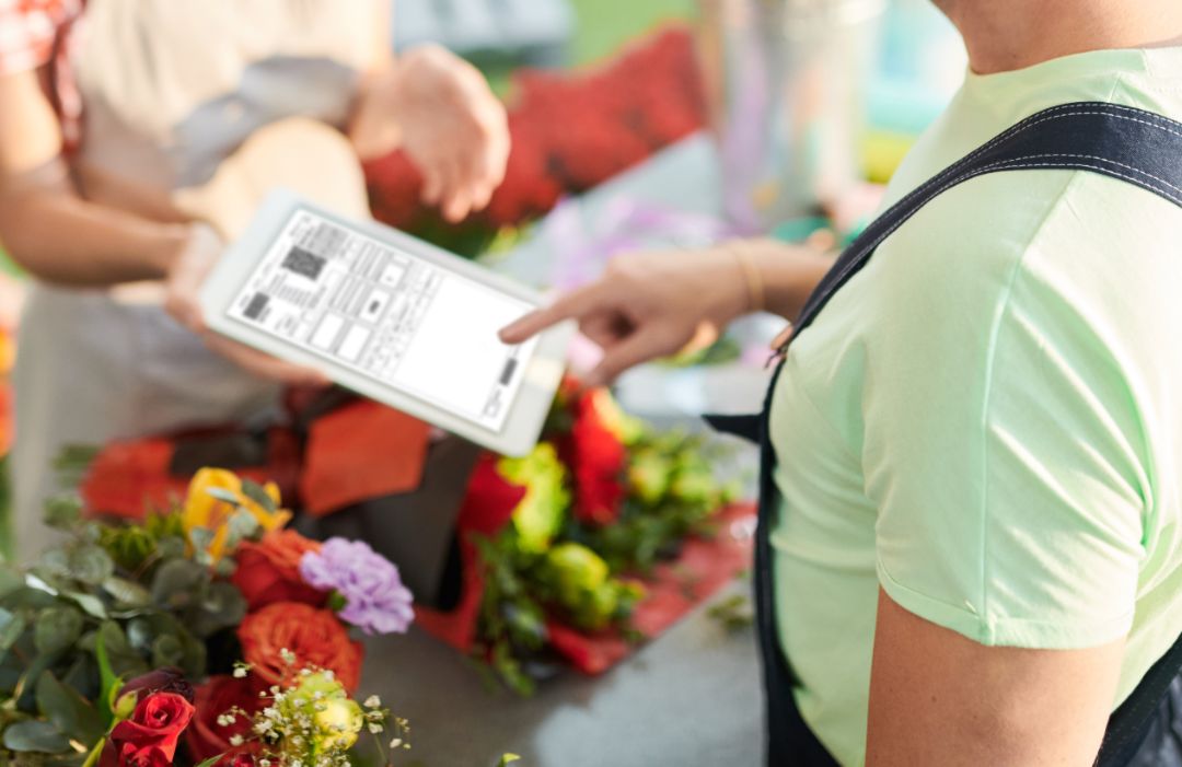 High angle portrait of delivery guy inputting order info to digital tablet while standing in small flower shop, copy space