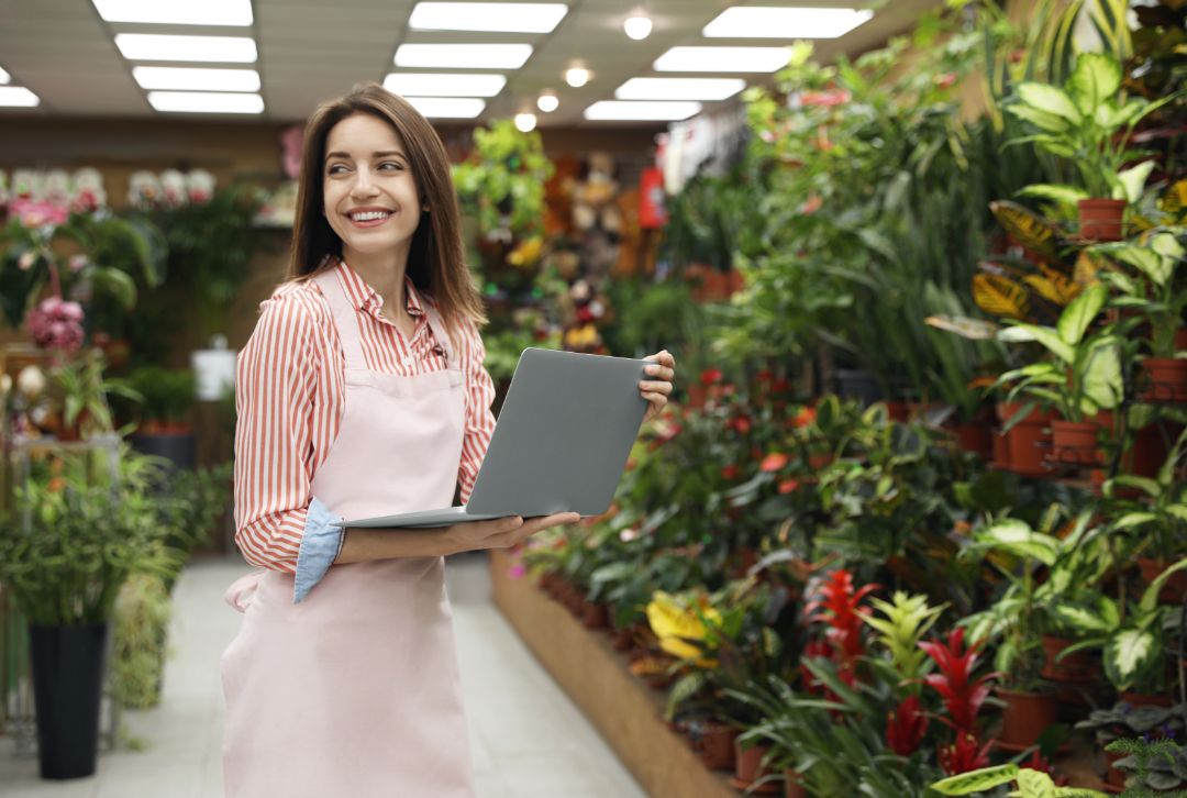 Young business owner with laptop in flower shop. Space for text